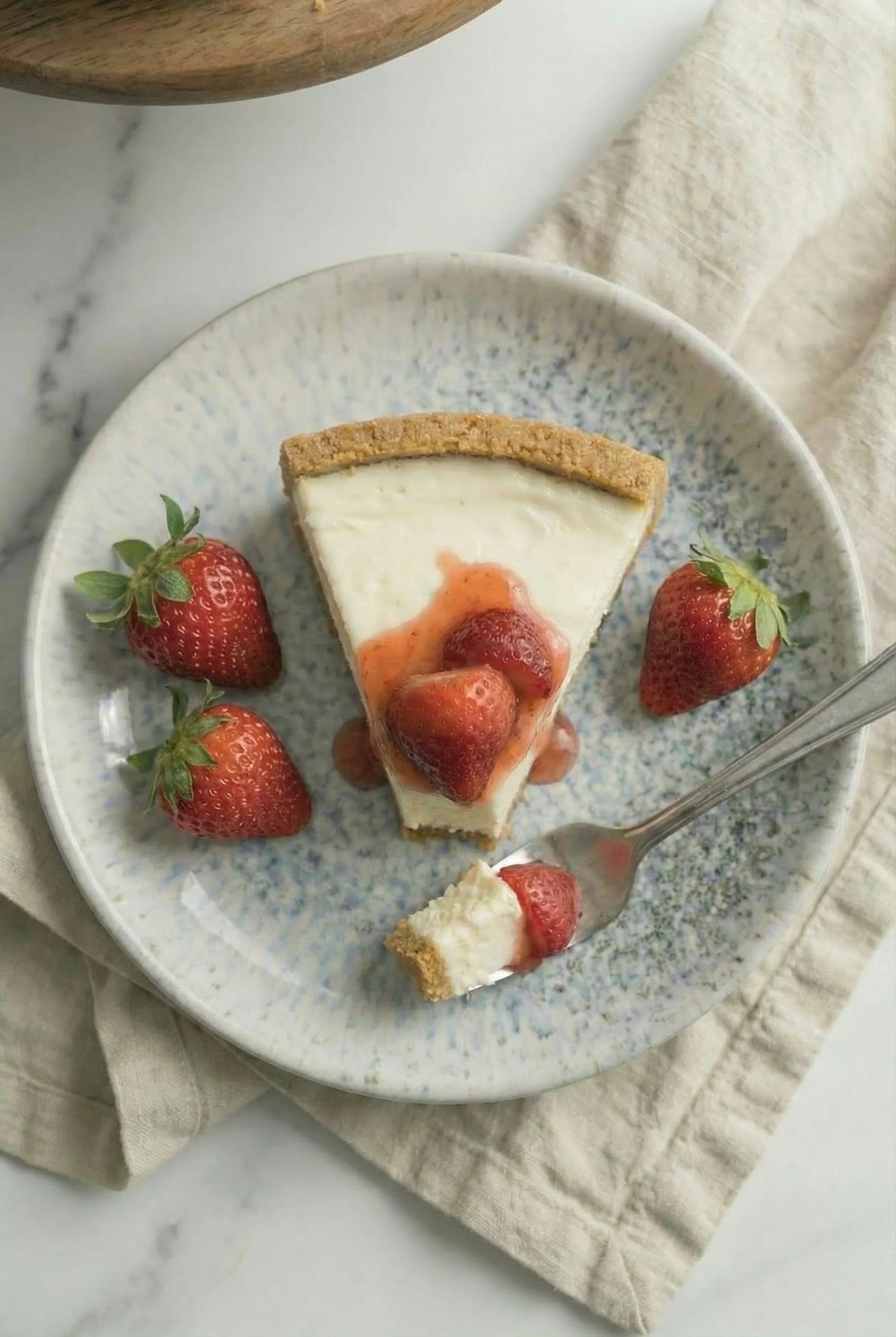 Creamy no-bake cheesecake slice topped with fresh strawberries and strawberry sauce on a ceramic plate.