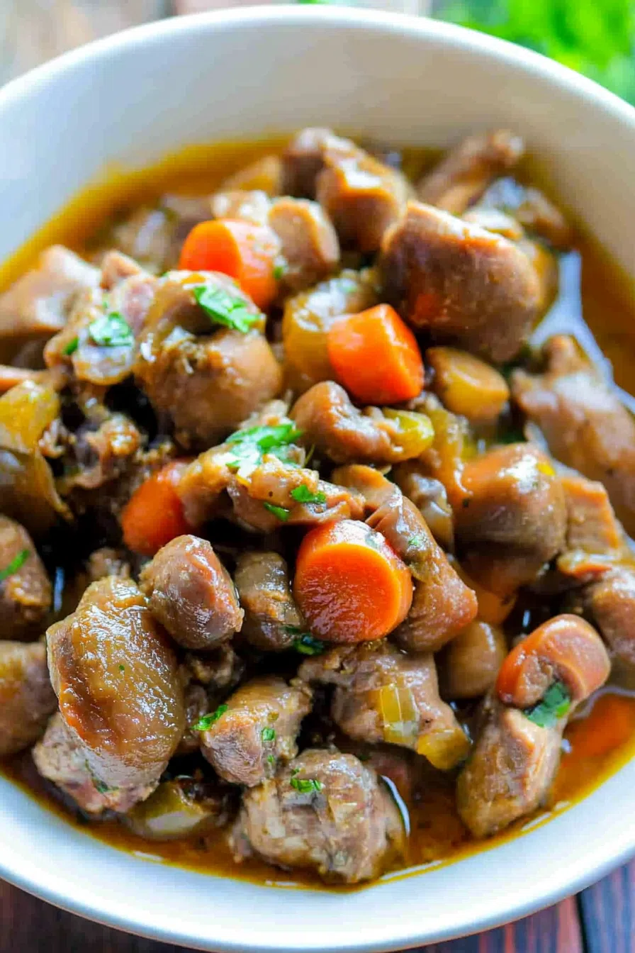 Close-up of tender braised chicken hearts and gizzards, garnished with fresh herbs, served on a white plate.