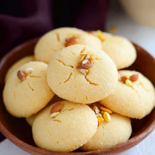 A serving platter with a stack of Nankhatai cookies, garnished with saffron strands and cardamom pods.