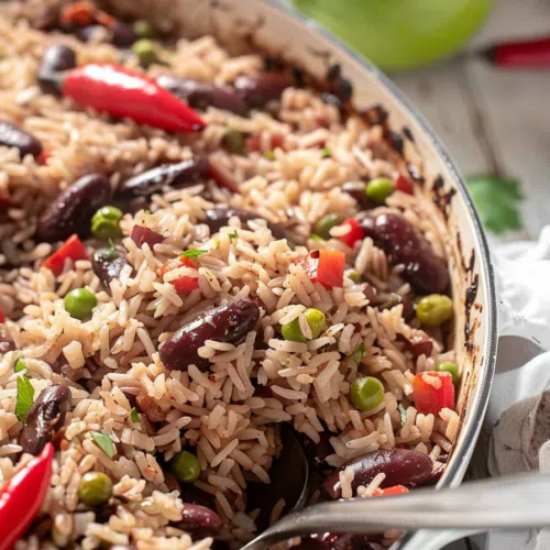 A skillet filled with perfectly cooked rice and peas, accented by bright red chili peppers and fresh herbs.