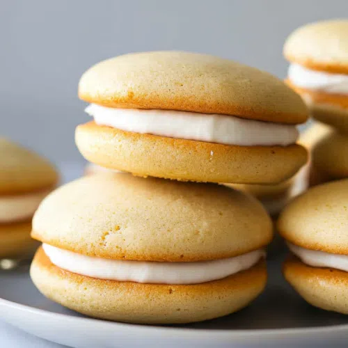 A close-up of two whoopie pies filled with creamy vanilla frosting, stacked on a plate.