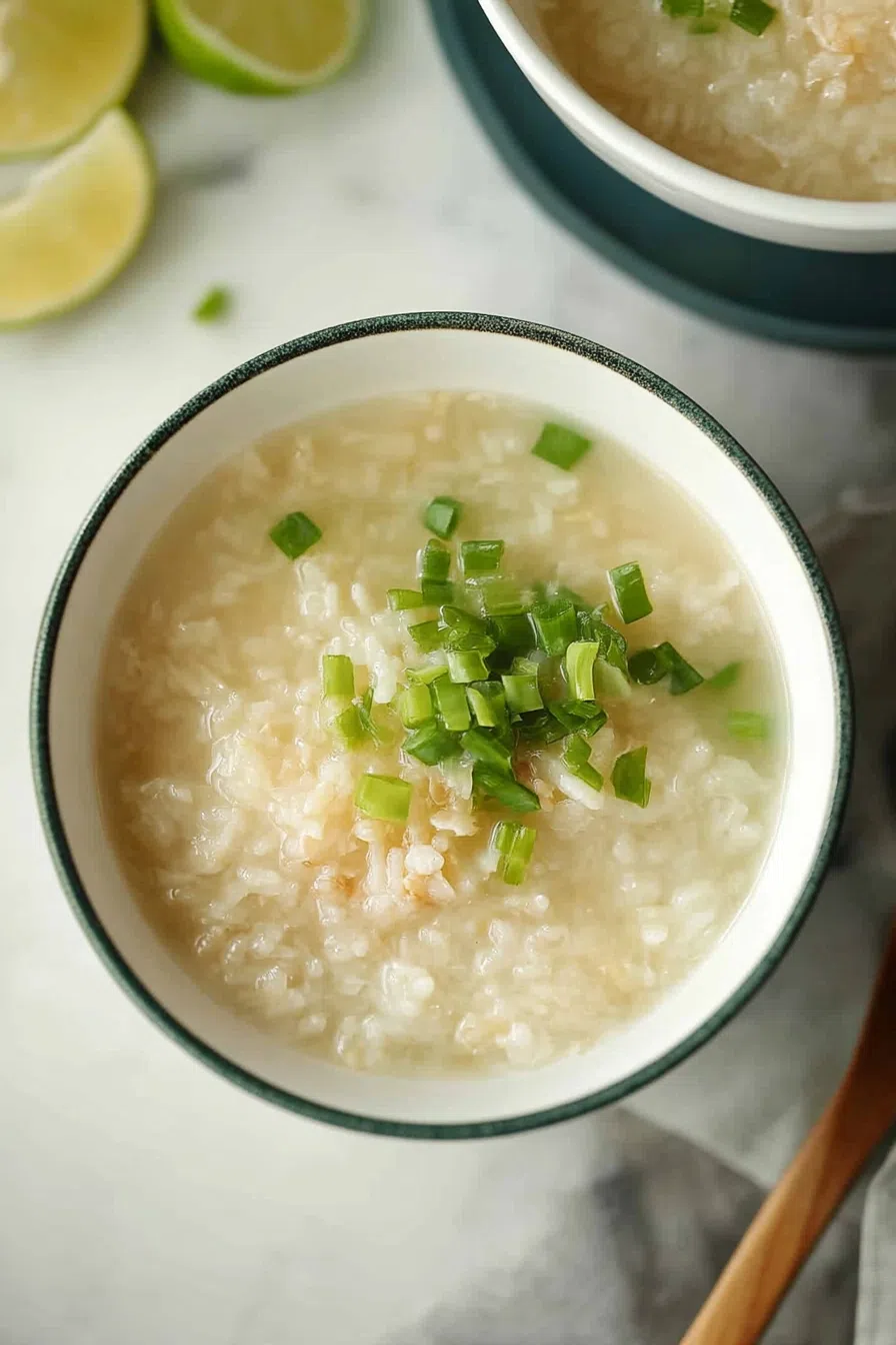 Bowl of creamy rice porridge topped with chopped scallions and a drizzle of soy sauce.
