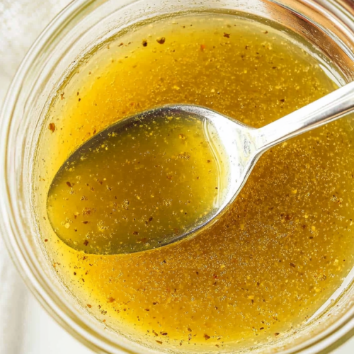 Close-up of a spoon scooping a tangy dressing in a bowl.
