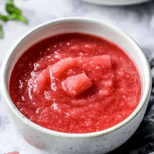 A close-up of a thick, ruby-red sauce with a few chunks of rhubarb visible.
