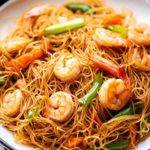 Close-up of mei fun noodles topped with plump shrimp and colorful bell peppers.