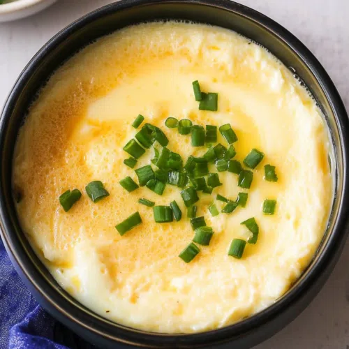 A bowl of fluffy steamed eggs garnished with chopped green onions.