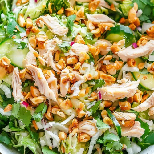 Close-up of a colorful chicken salad topped with crushed peanuts and chili slices.