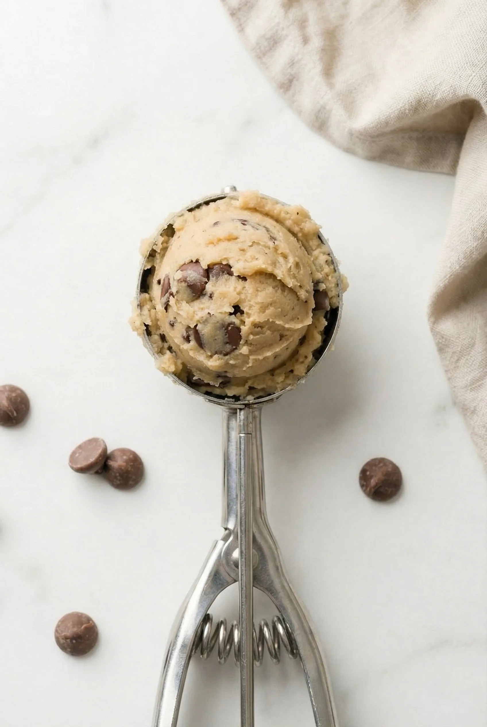 Close-up of a rounded scoop of chocolate chip cookie dough resting in a metal cookie scoop