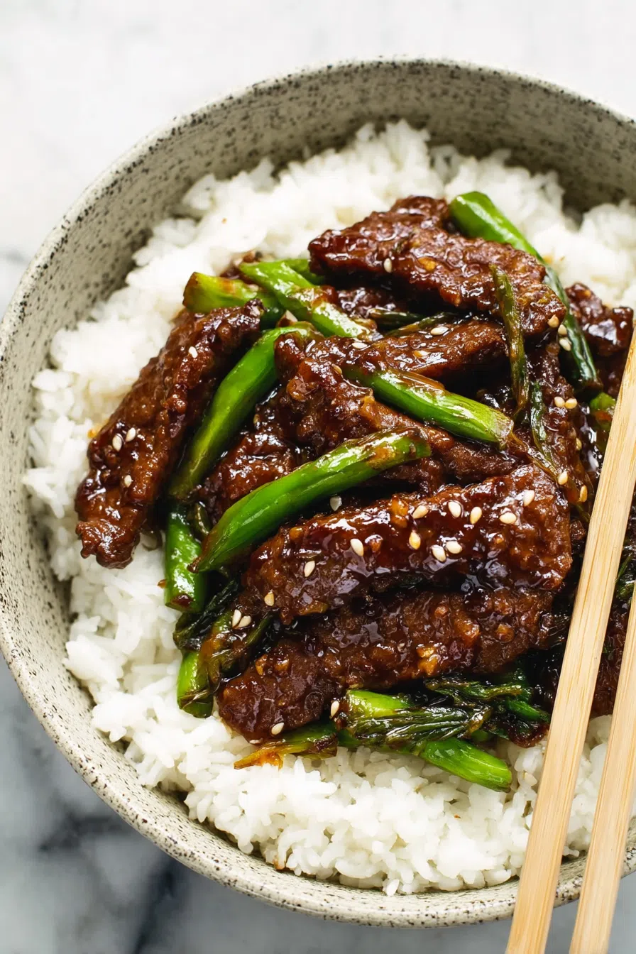 Dinner plate featuring saucy meat and steamed white rice, arranged neatly with a sprinkling of sesame seeds.