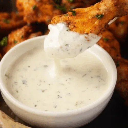 Overhead shot of dipping sauce next to a plate of crispy wings.