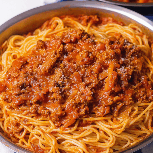 Side view of a plated pasta dish with visible herbs and a thick tomato topping.