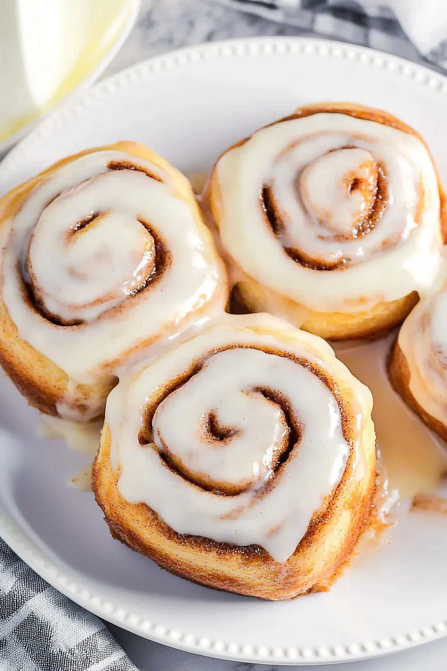 Freshly baked swirled pastries topped with glossy vanilla icing on a white plate