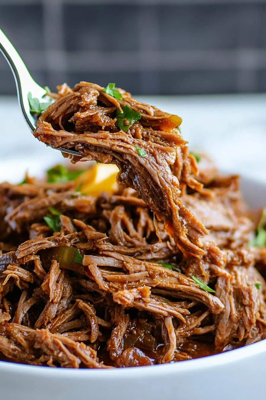 Close-up of shredded meat with rich sauce, garnished with chopped parsley.