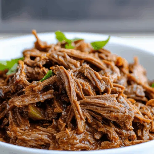 Close-up of tender strands of slow-cooked meat, garnished with fresh herbs.