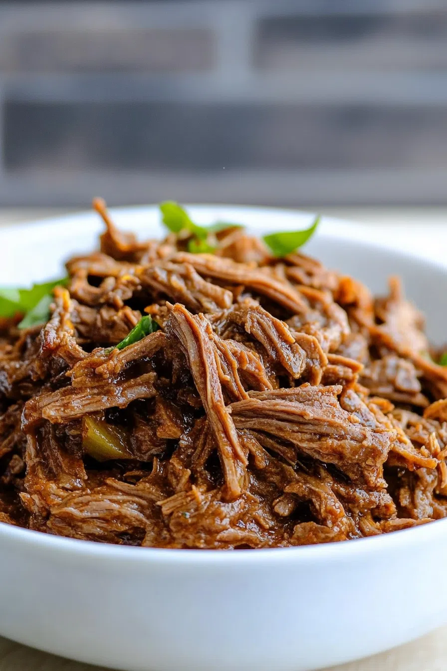 Close-up of tender strands of slow-cooked meat, garnished with fresh herbs.