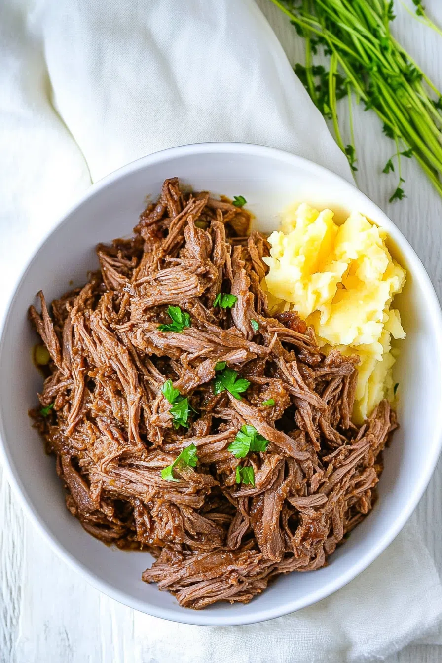 Tender pulled meat served on a plate with mashed potatoes and gravy.