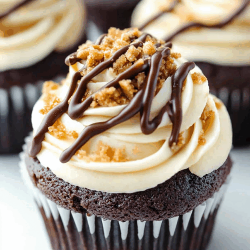 A single cupcake on a white plate with layers of frosting and toasted topping