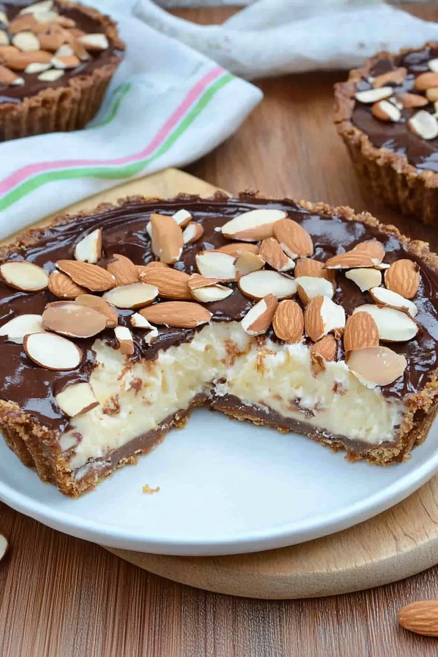 Close-up of a rich, glossy ganache topping with toasted almonds and coconut flakes.
