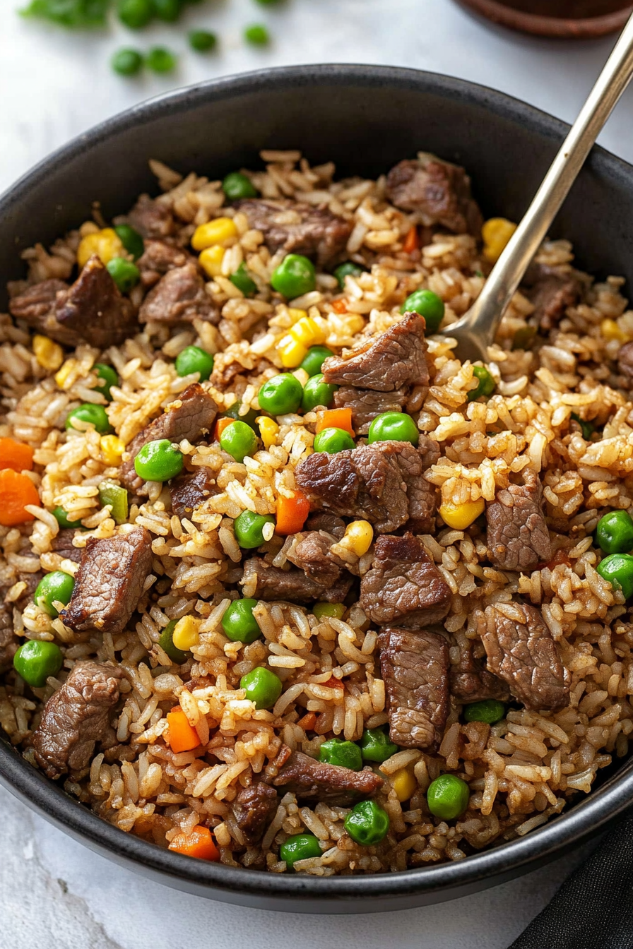 Skillet filled with golden fried rice, colorful vegetables, and tender beef strips.