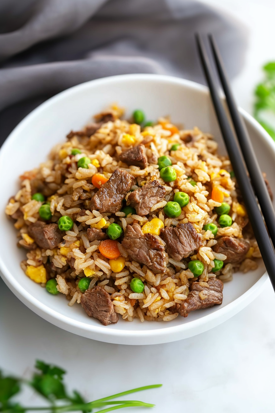 Chopsticks resting on a plate of steaming rice stir-fry with vegetables.