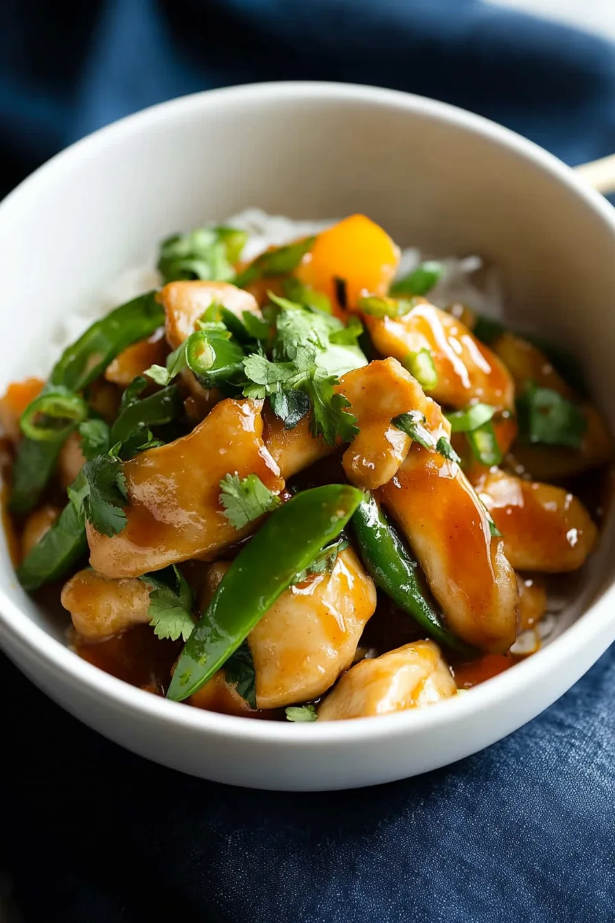 Stir-fried chicken with colorful bell peppers and a glossy sauce on a white plate