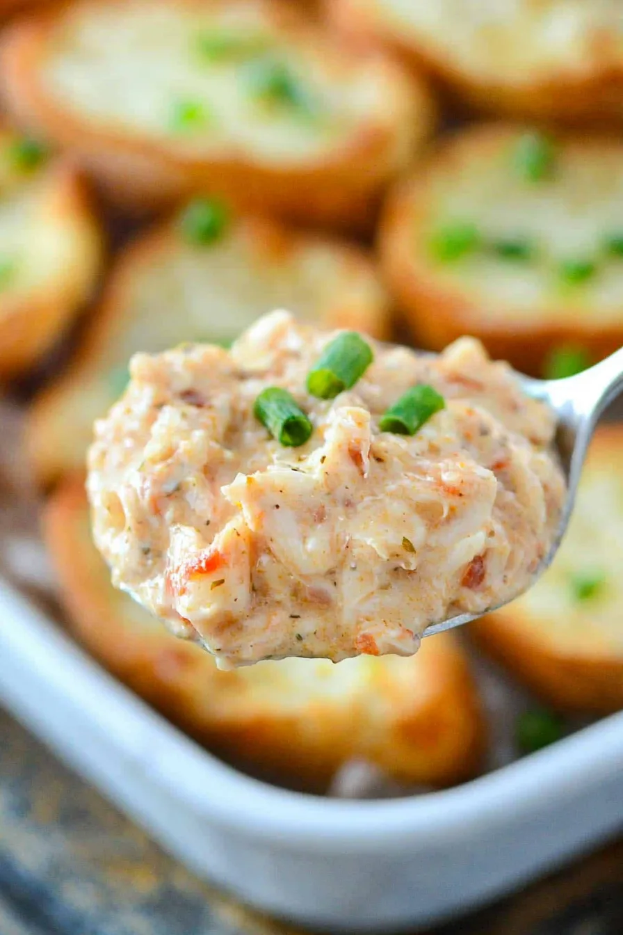 Close-up of crab dip being scooped onto a cracker.