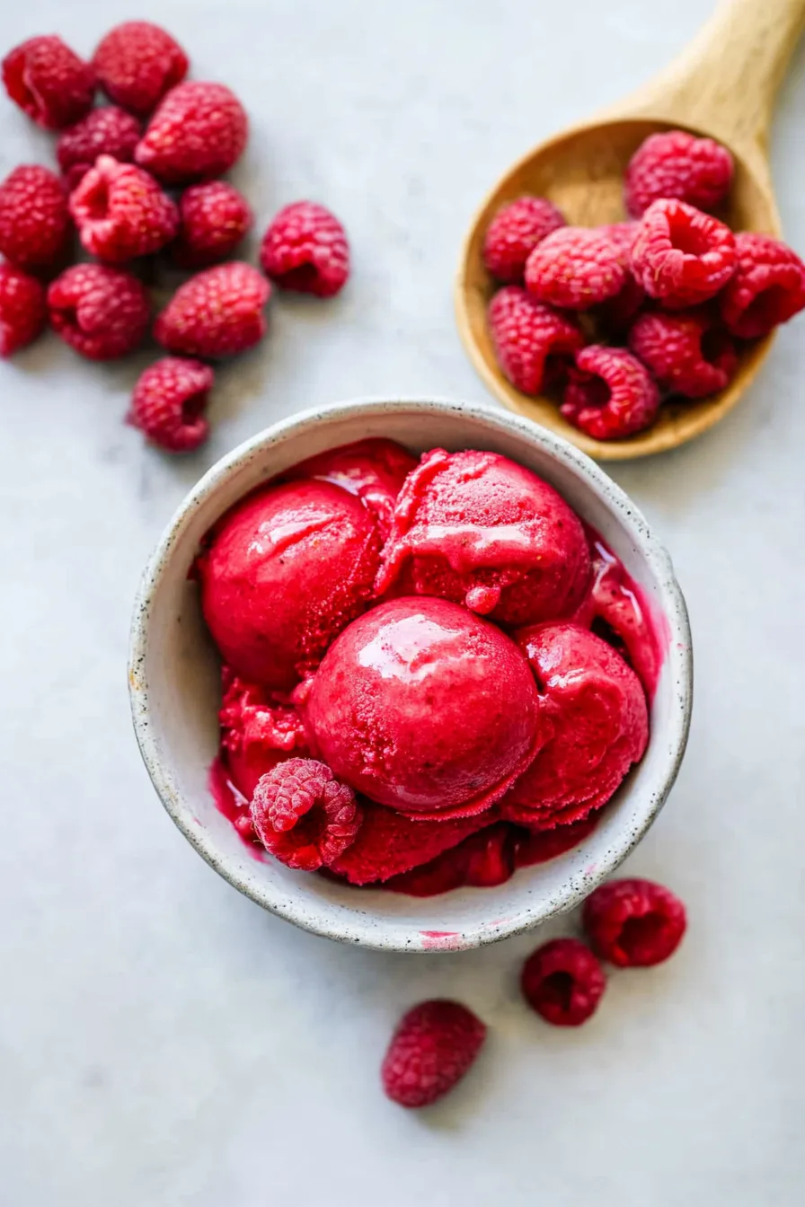 A scoop of bright pink frozen dessert in a small white bowl with a mint garnish.