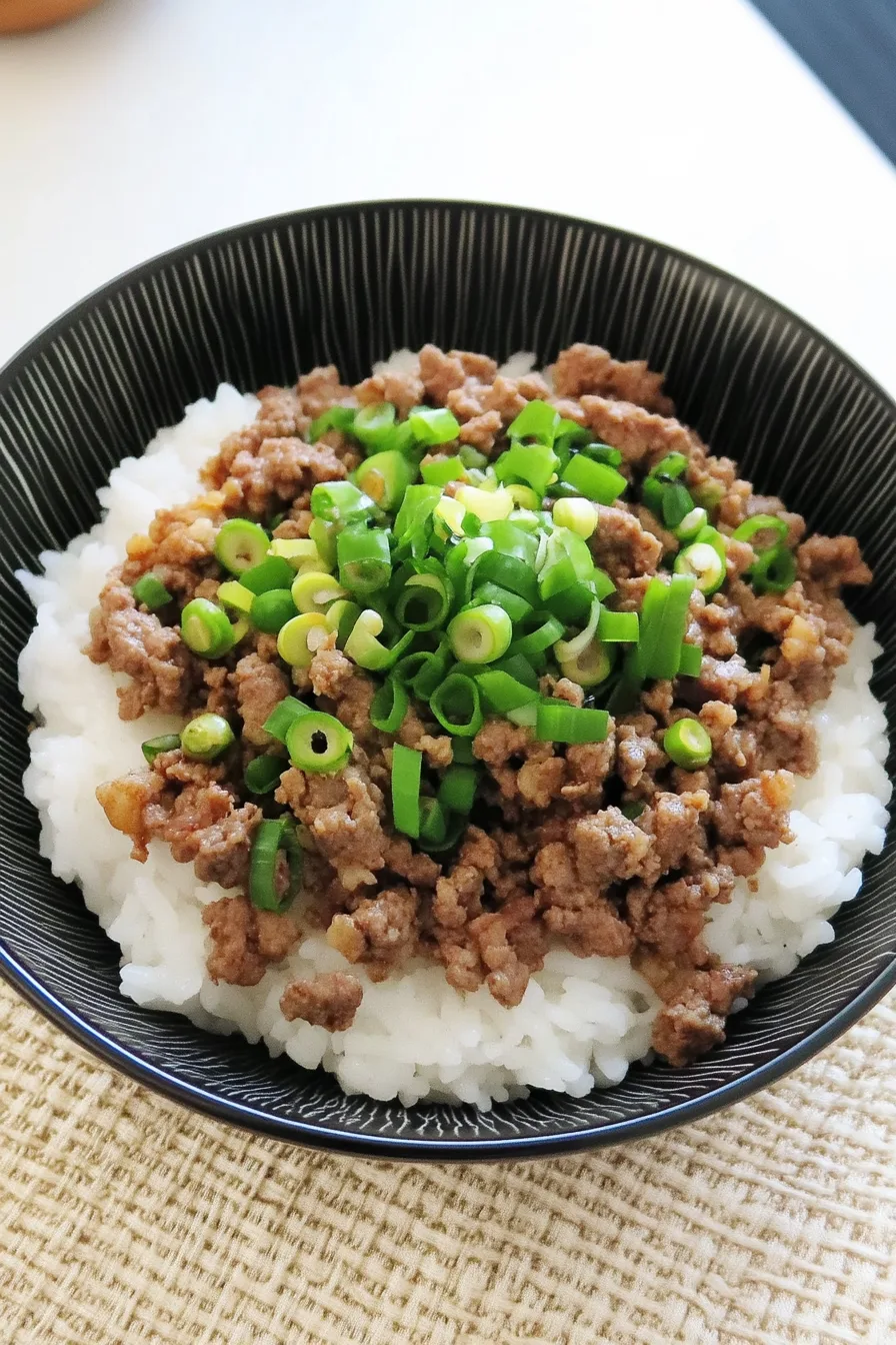 Bowl of ground beef donburi topped with fresh ginger and scallions