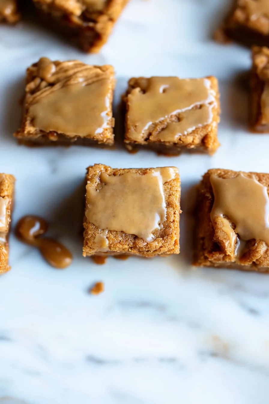 A square of blondie topped with glossy maple glaze and apple pieces on a dessert plate.