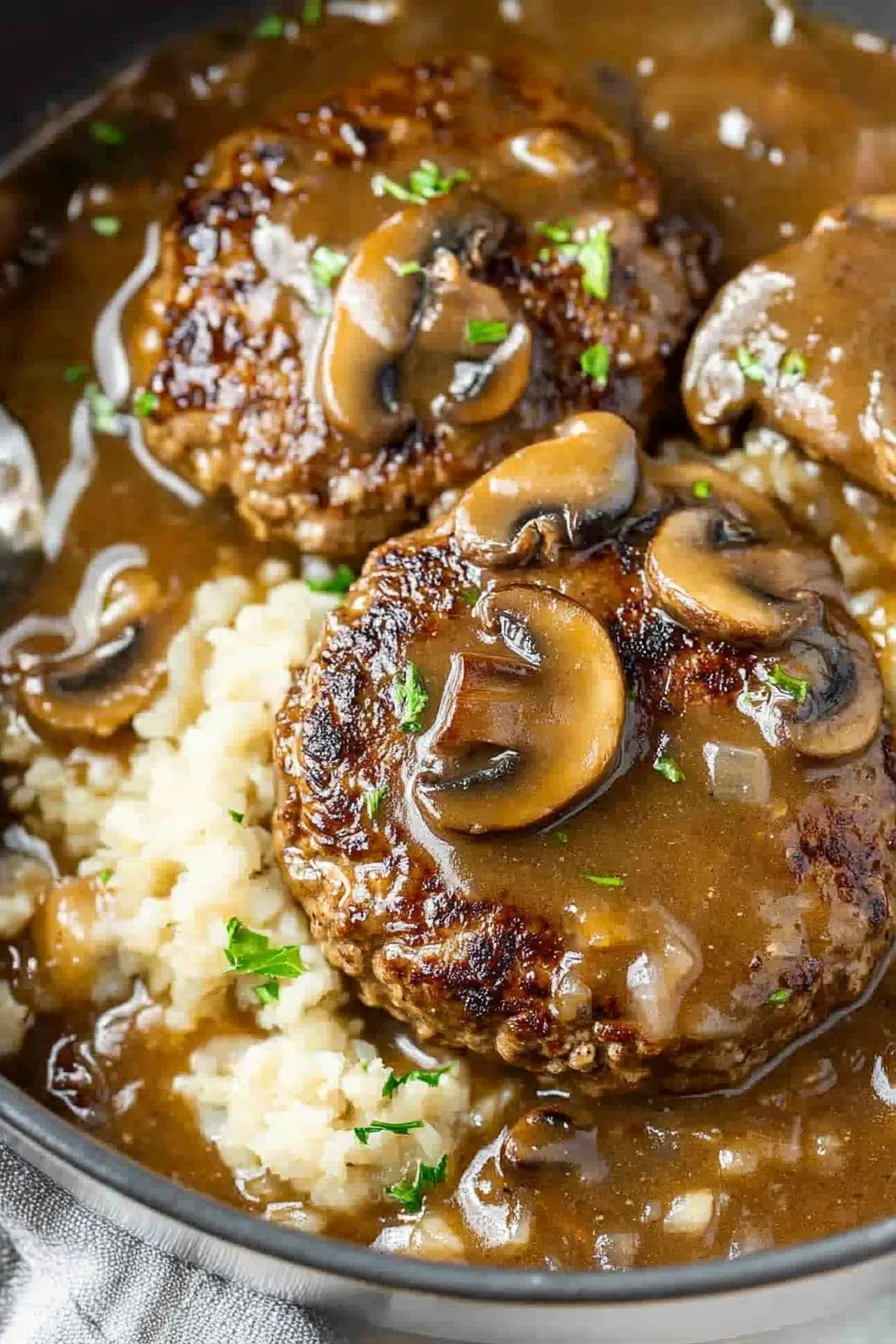 Close-up of tender steak patties smothered in brown onion gravy with mushrooms.