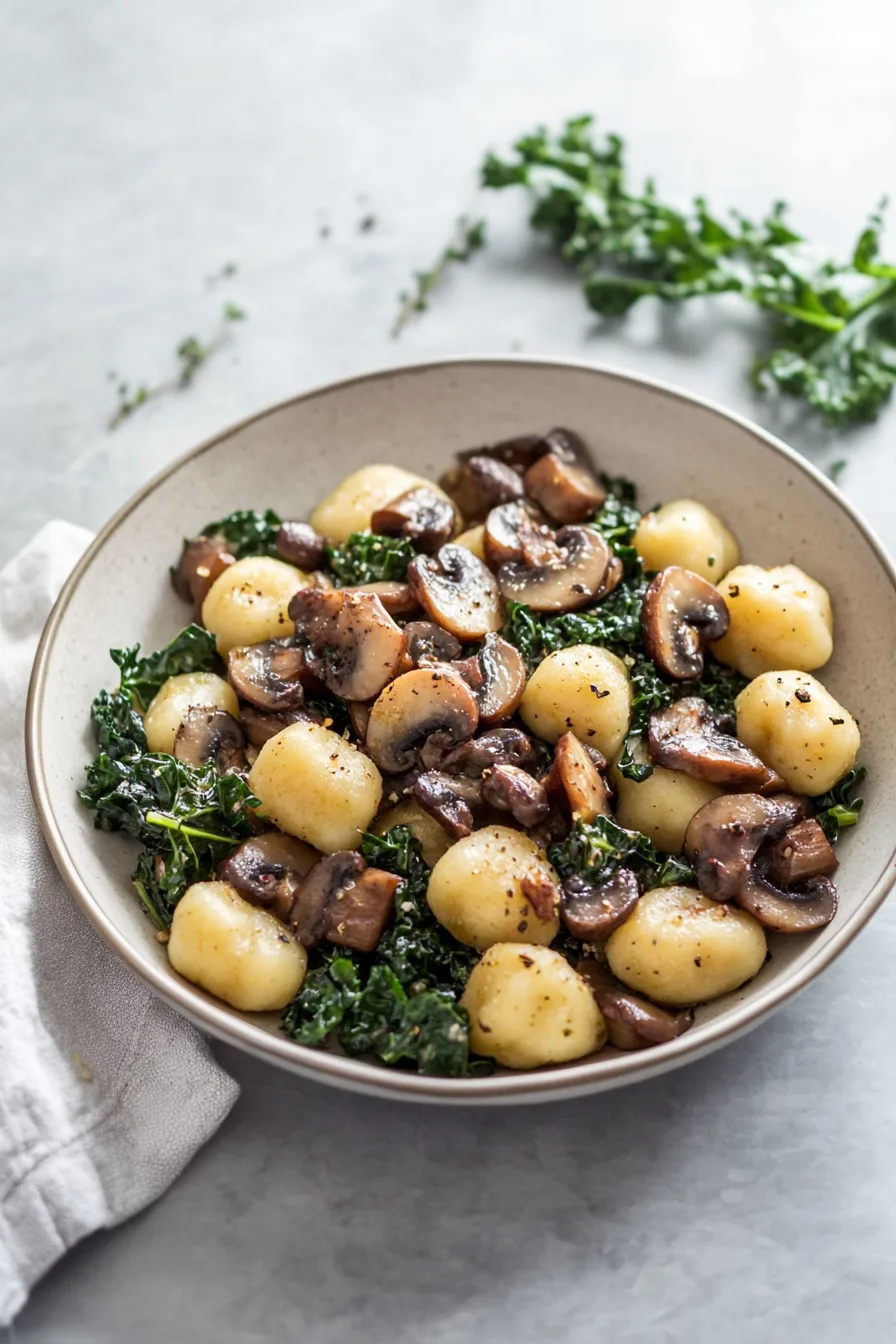 Crispy gnocchi and sausage pieces mixed with tender kale in a white serving bowl.