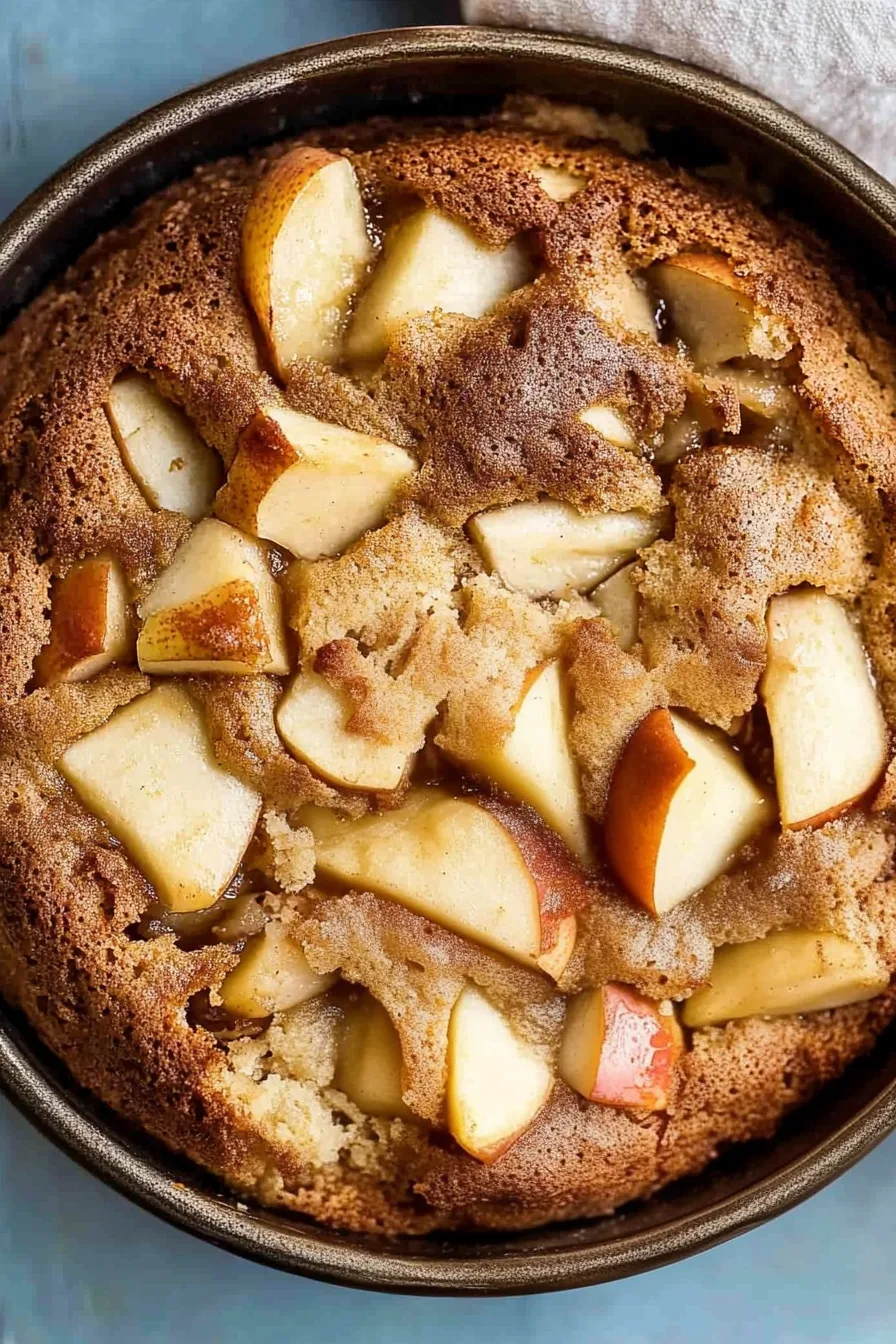 Close-up of a warm dessert filled with baked apple pieces and a soft, caramelized crust.
