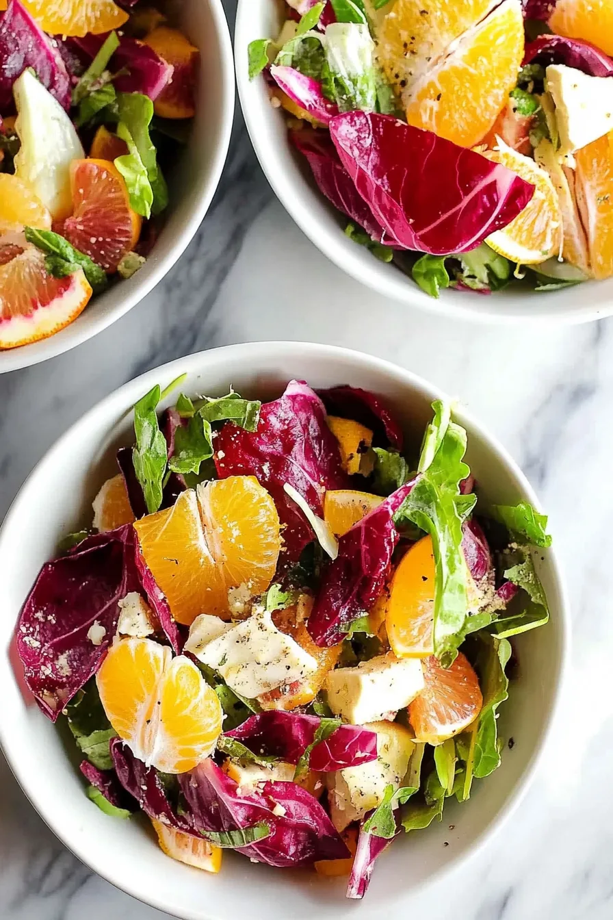 Vibrant salad with orange slices, radicchio, and shaved cheese on a marble surface.