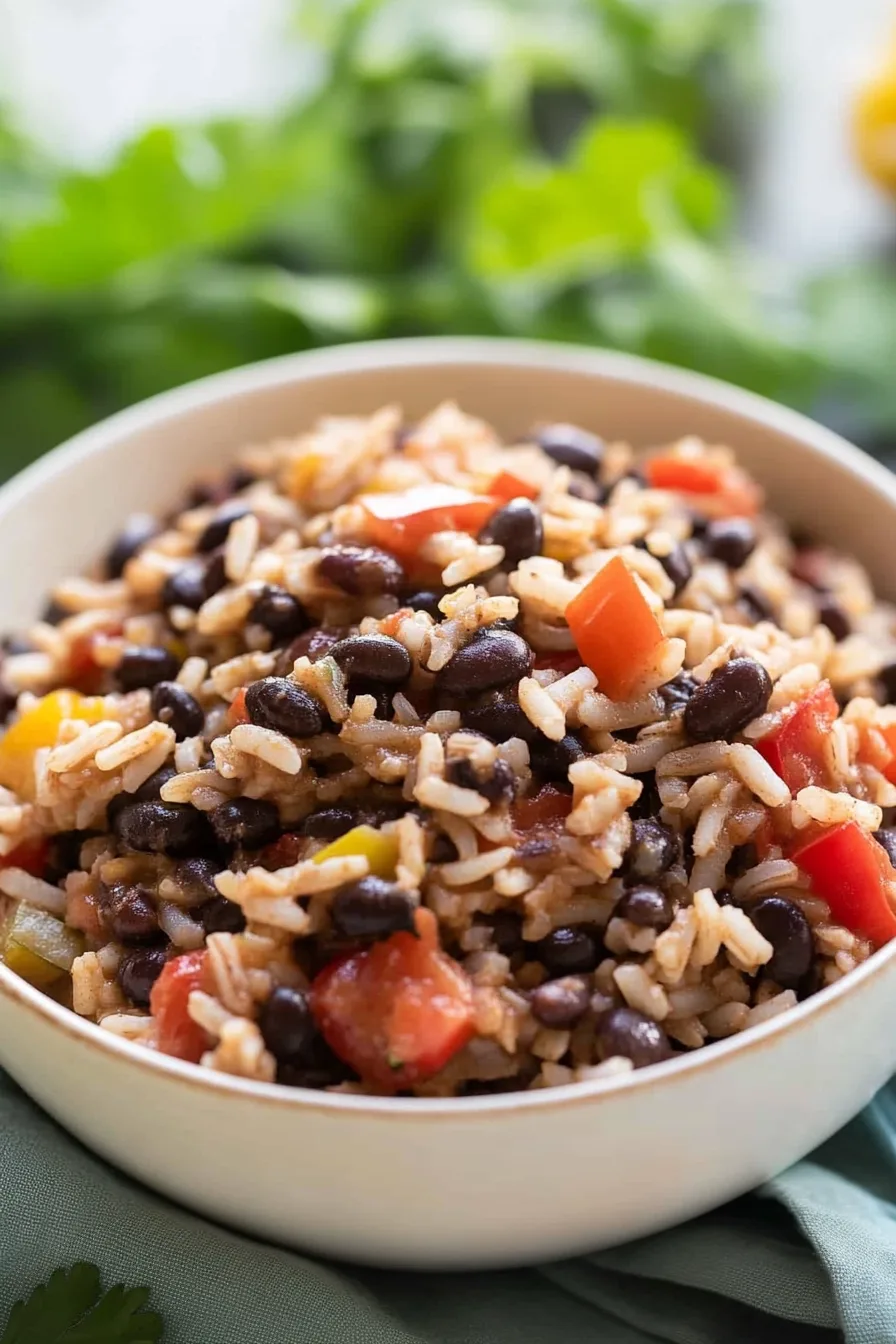 Close-up of steaming black beans and rice with sautéed vegetables on top.