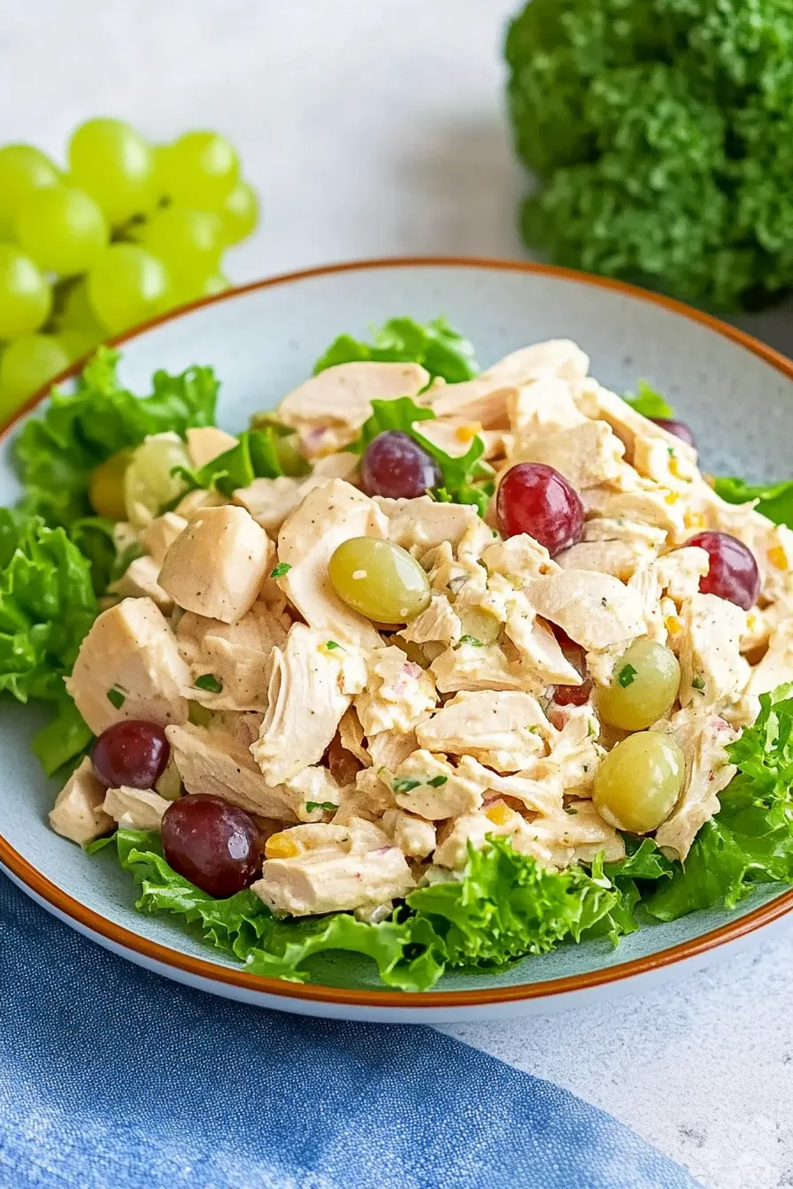 Bowl of creamy chicken mixture dotted with whole grapes and placed on crisp lettuce.