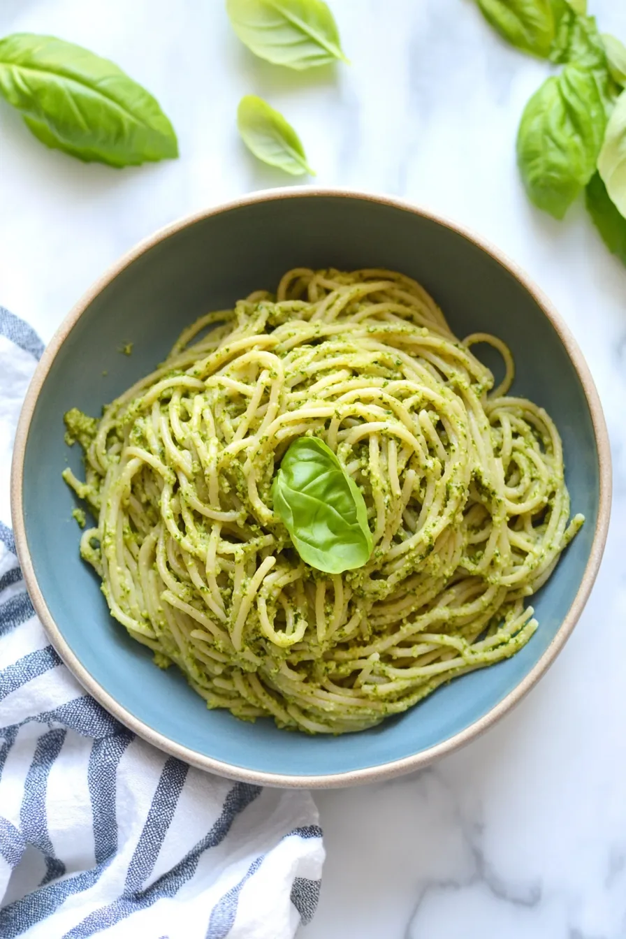 Simple pasta dish with a rich green coating and a single basil leaf on top.