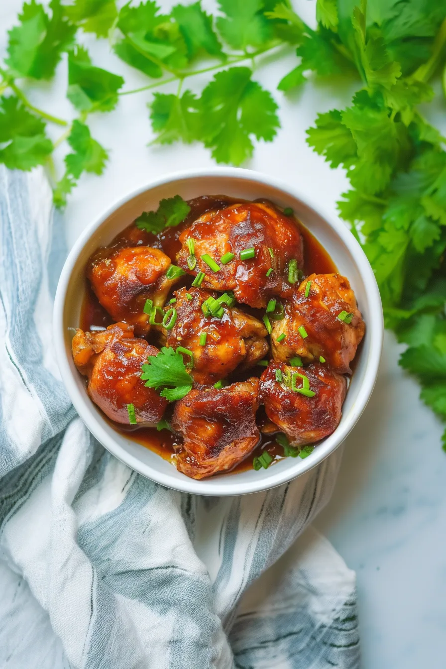 Plated chicken in a rich amber glaze, garnished with fresh green herbs.
