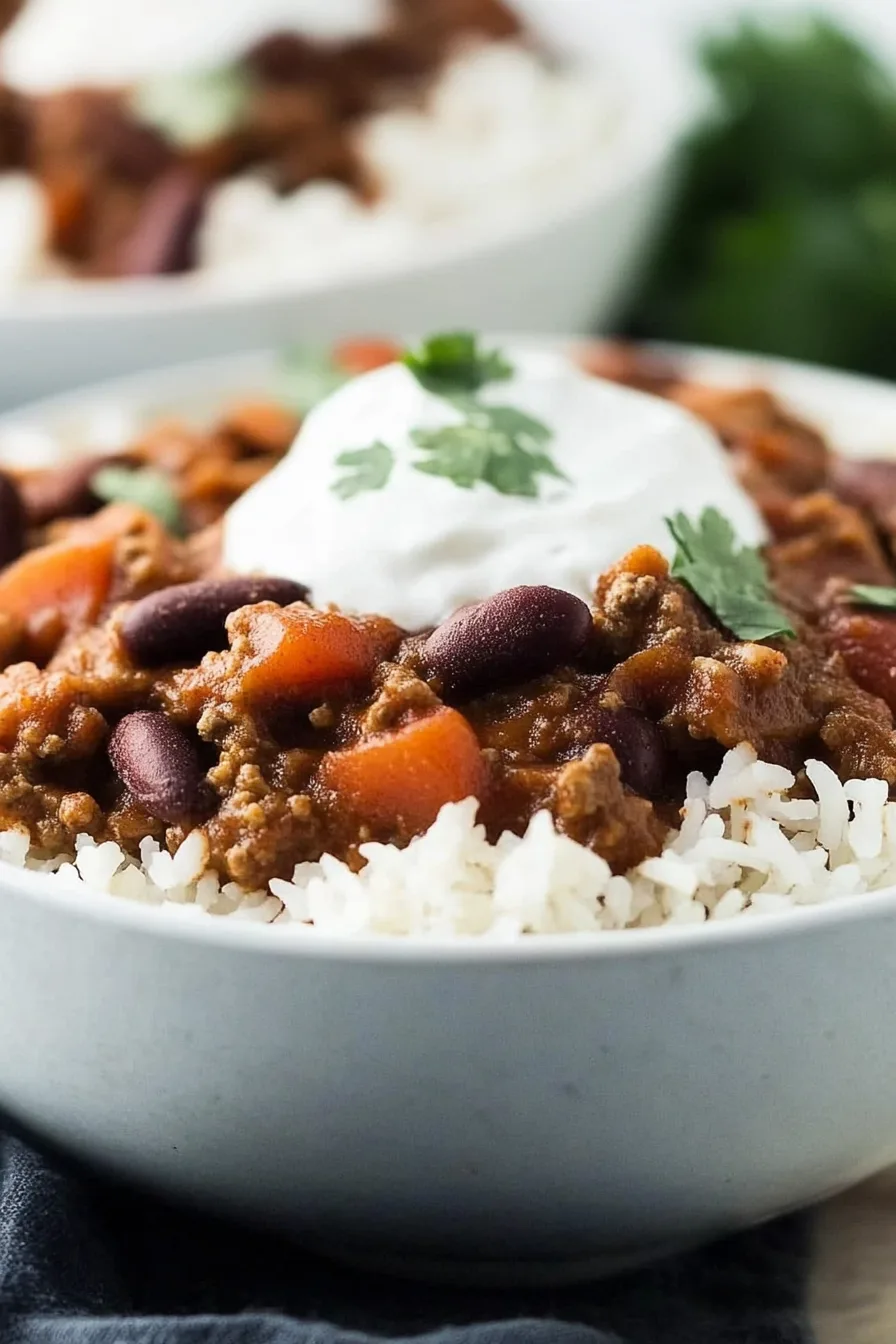Close-up of savory chili with beans and diced tomatoes served over fluffy rice.