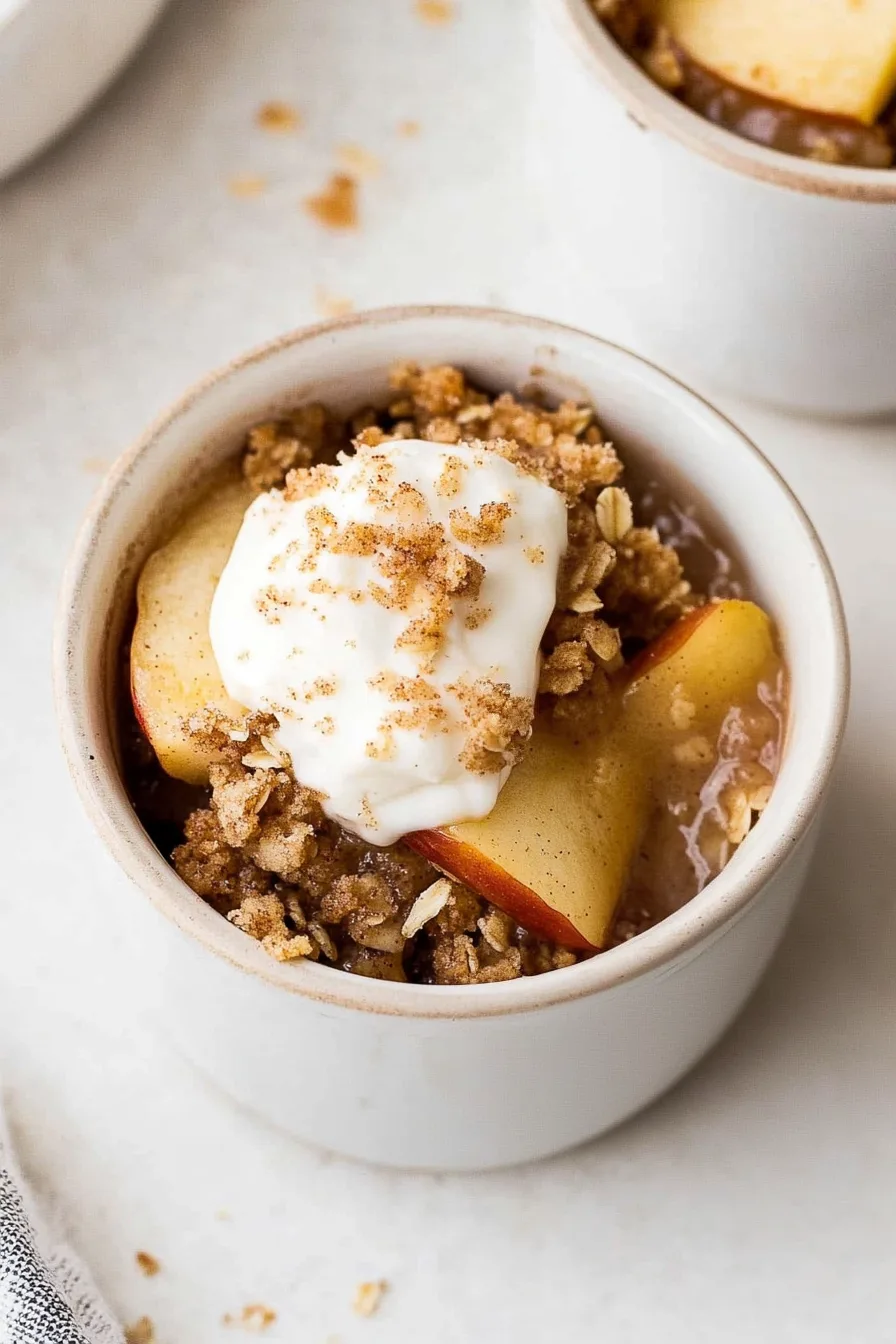 Close-up of baked apples and oat crumble with whipped topping.