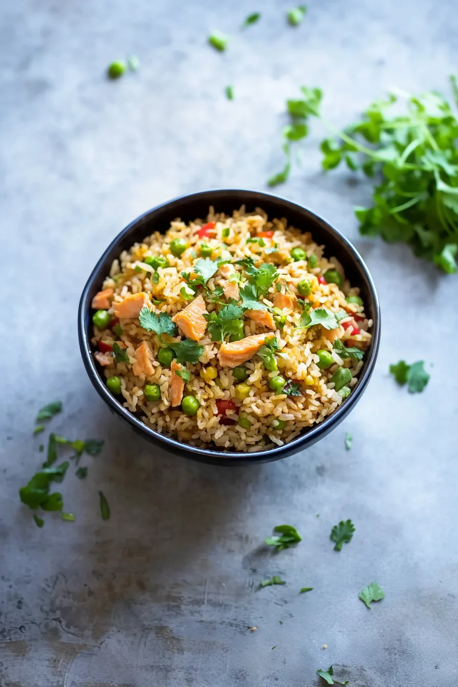 Overhead shot of a finished fried rice dish featuring salmon and mixed veggies in a shallow bowl.
