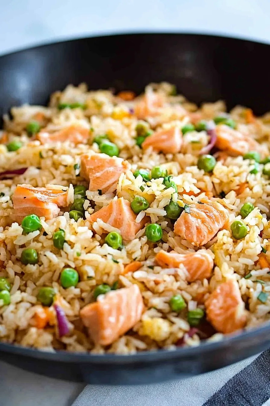 Close-up of a hearty rice dish with tender salmon pieces and green onions sprinkled on top.
