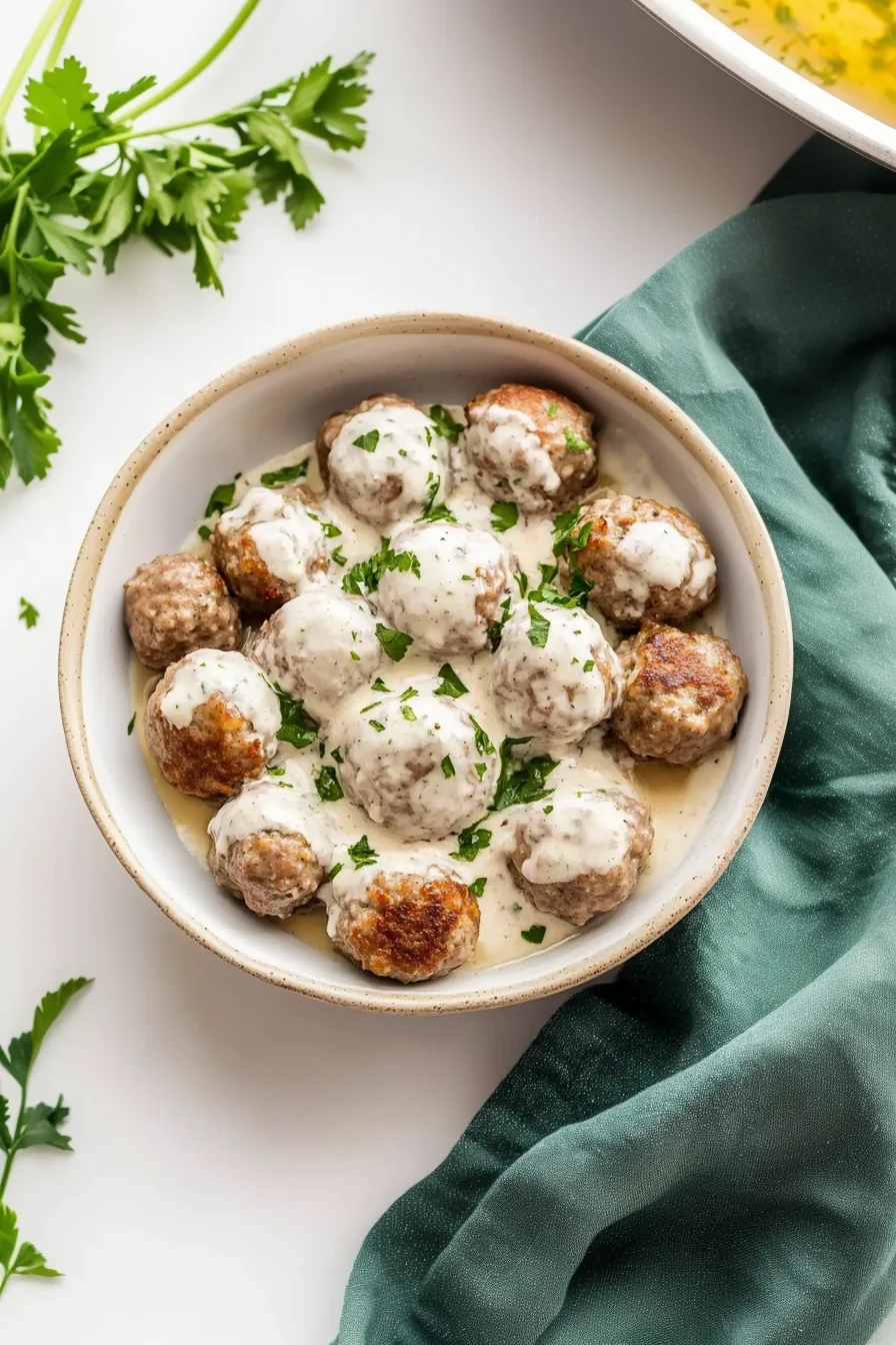 Homestyle comfort dish featuring meatballs topped with white sauce and parsley.