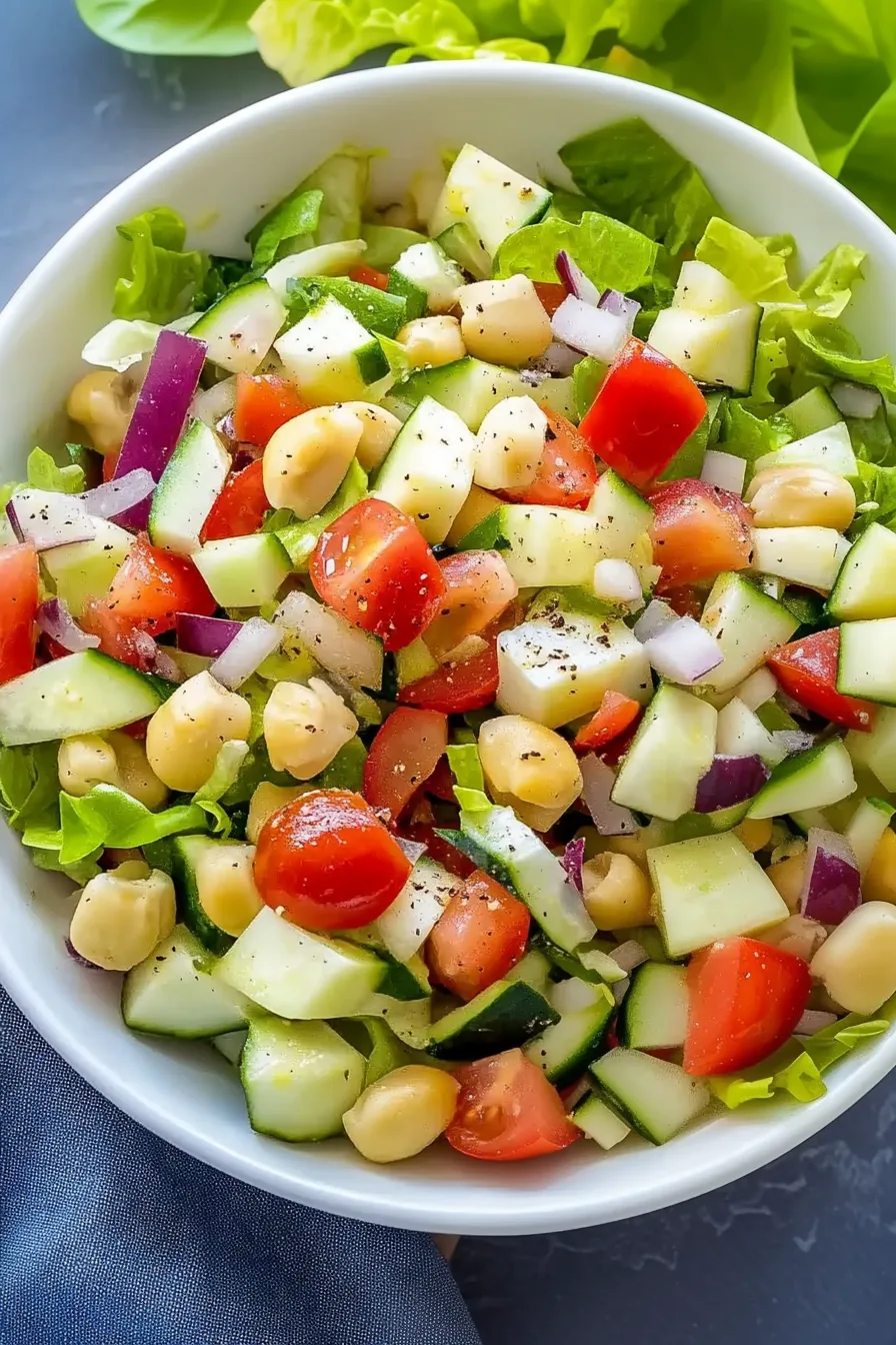 Colorful bowl of chopped lettuce, tomatoes, olives, and sliced red onions tossed with dressing.