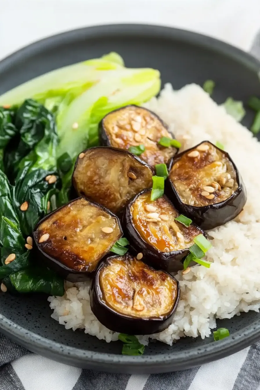 Close-up of caramelized eggplant topped with chopped green onions on a white serving plate.