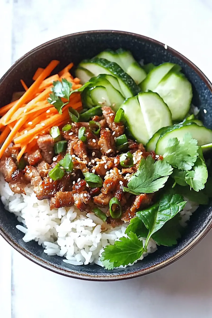 Close-up of a rice bowl with savory pork pieces, sesame seeds, green onions, and cilantro.