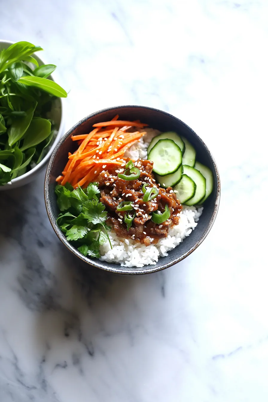 Overhead view of a fresh and vibrant rice bowl with seasoned pork and sliced vegetables.