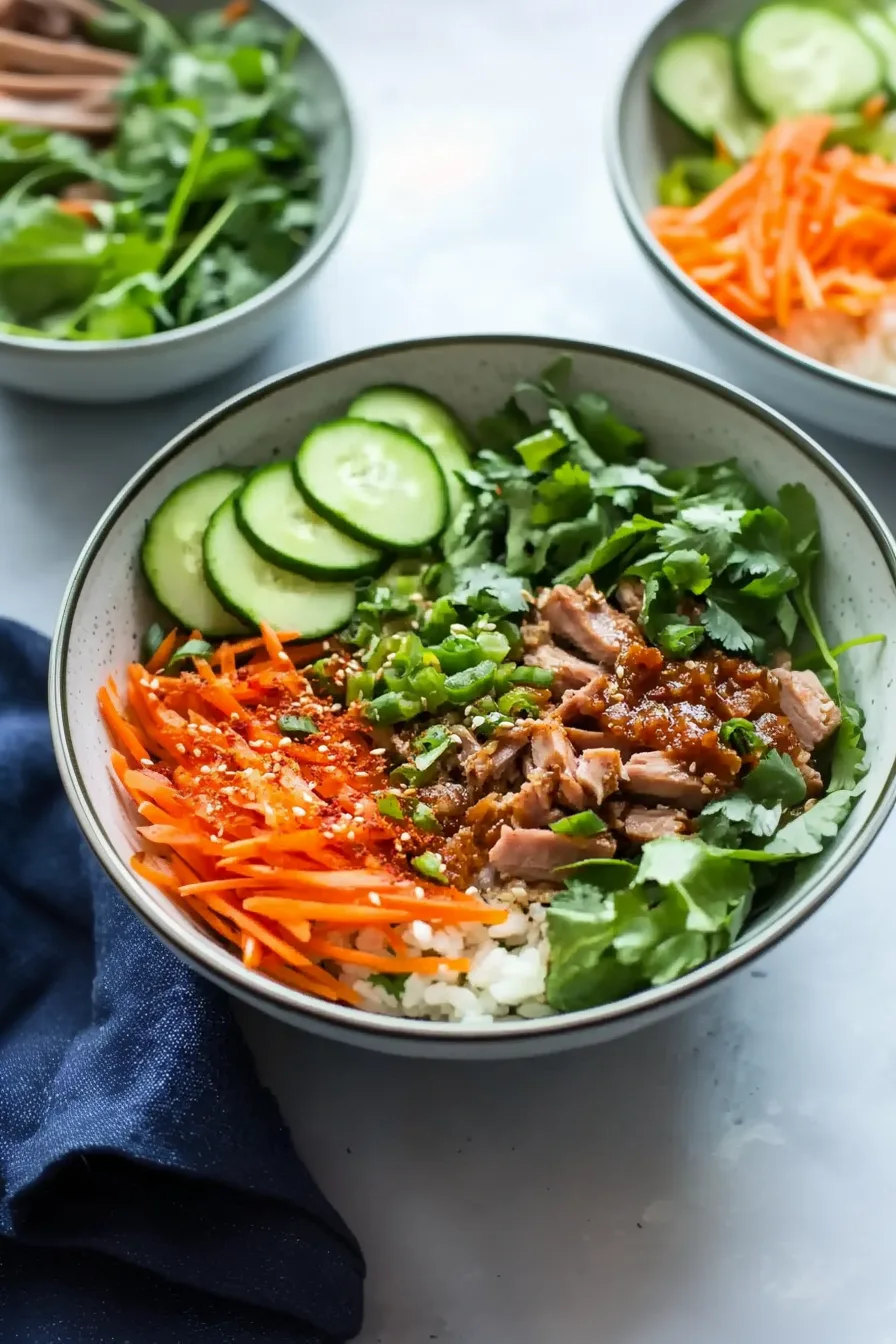 Hearty rice bowl with flavorful pork and bright garnishes arranged neatly on top.