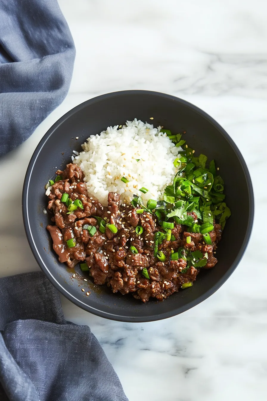 Overhead view of a hearty beef-and-rice bowl with a glossy sauce and fresh green toppings.