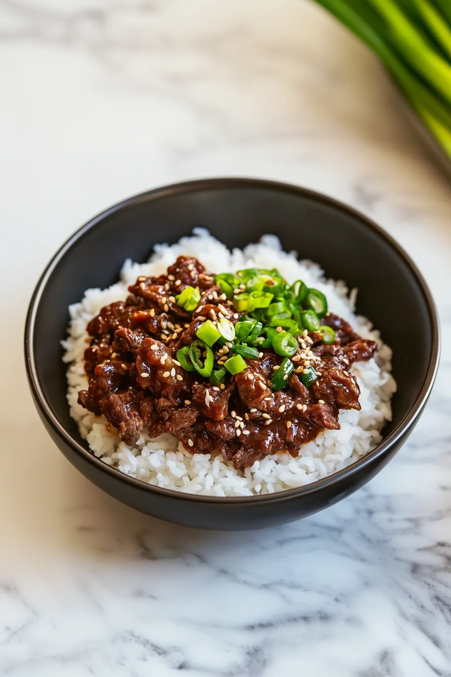 A bowl of cooked white rice served with savory browned beef topped with sliced green onions and sesame seeds.