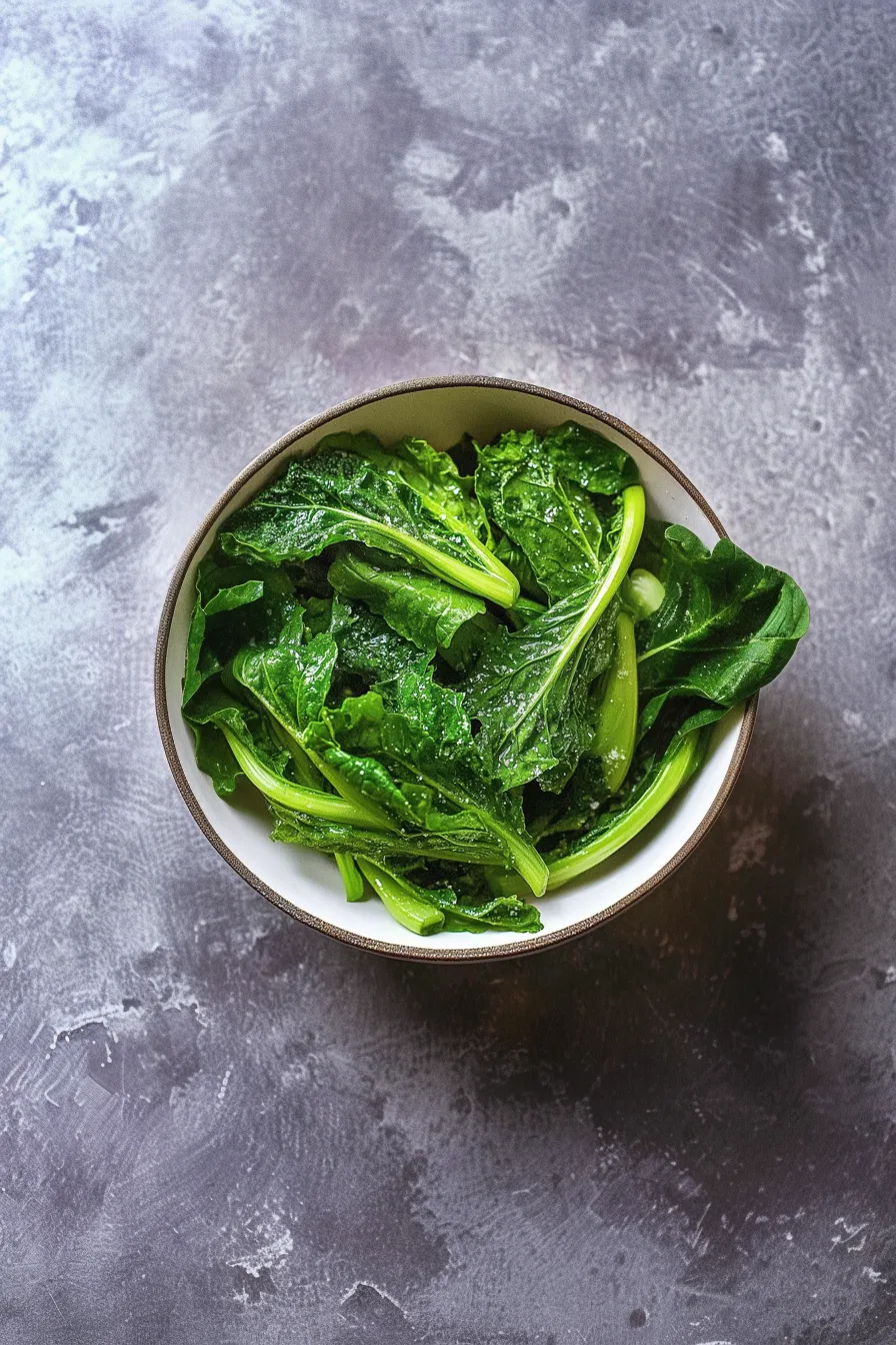 Cooked greens in a white ceramic bowl against a dark background.